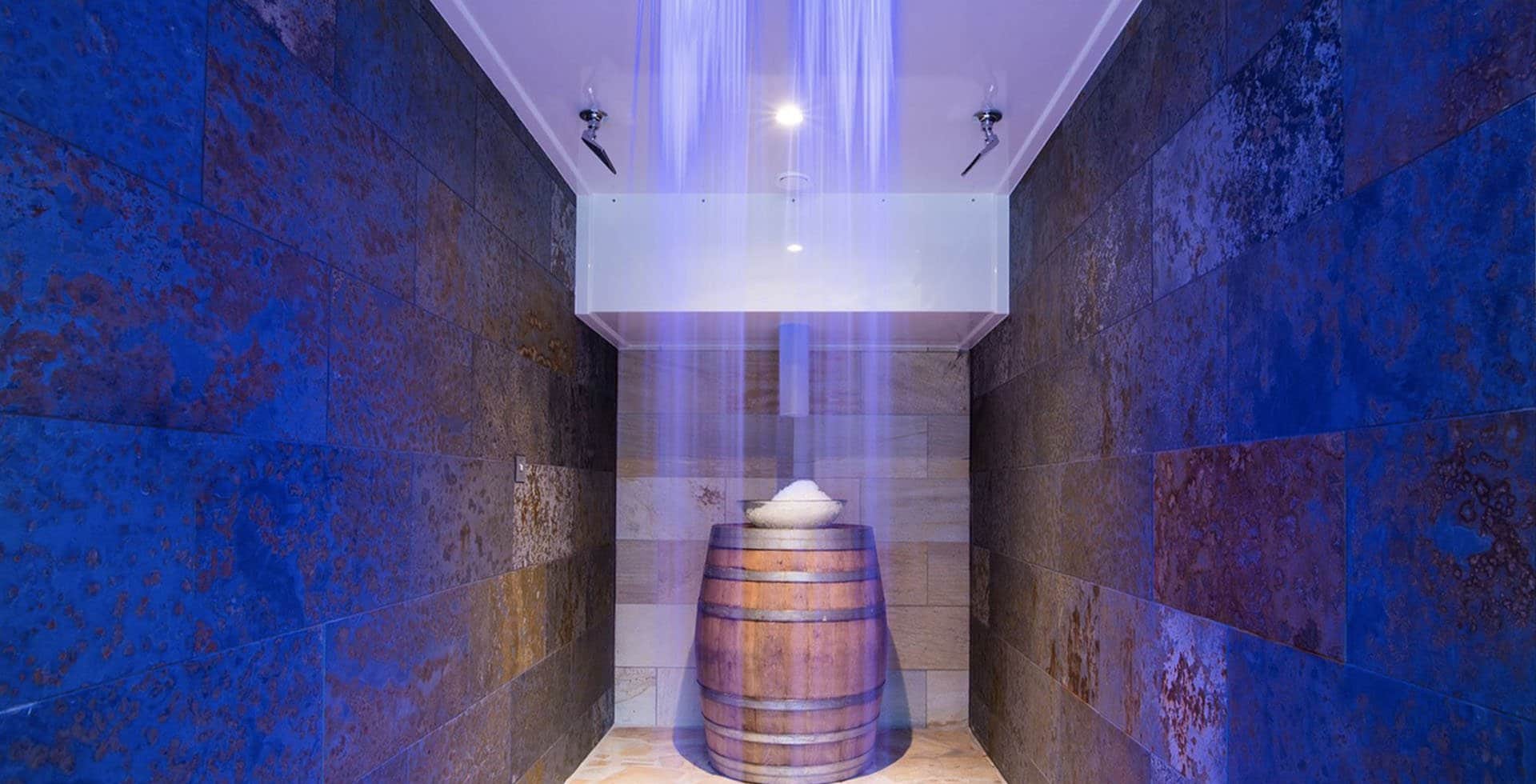 Experience shower with a wooden tipping bucket, rainfall head and blue-lit stone walls