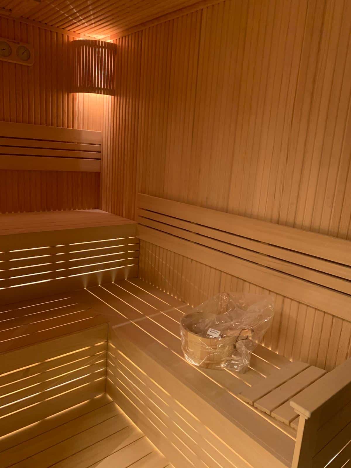 Newly built hotel sauna at Novotel Istanbul Bomonti: two tiers of slatted benches lit from below, slatted backrests, a slatted wall lamp and a thermometer and hygrometer on the wall