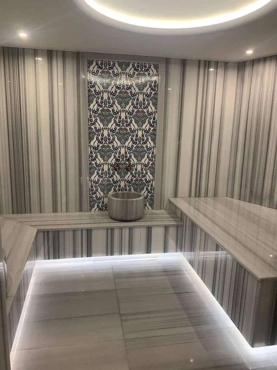 Hammam in the spa of Novotel Istanbul Bomonti: striped grey marble walls, a raised marble platform lit from underneath, a carved stone basin and a blue patterned tile panel
