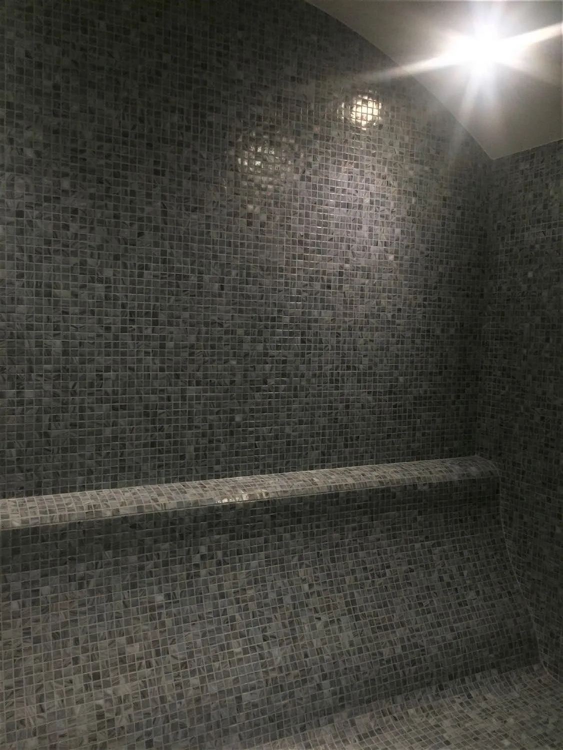 Dark mosaic steam room at Hilton Istanbul Maslak with a tiled bench running along the wall