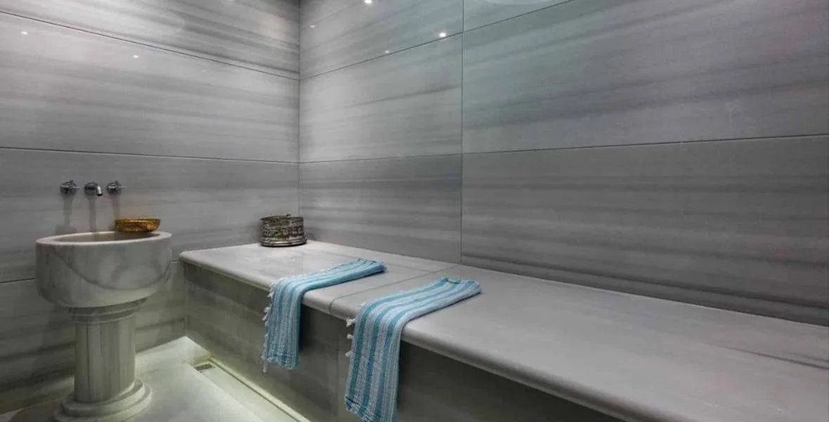 VIP hammam at Hilton Istanbul Maslak: a long marble bench, a carved marble basin and soft light along the wall base
