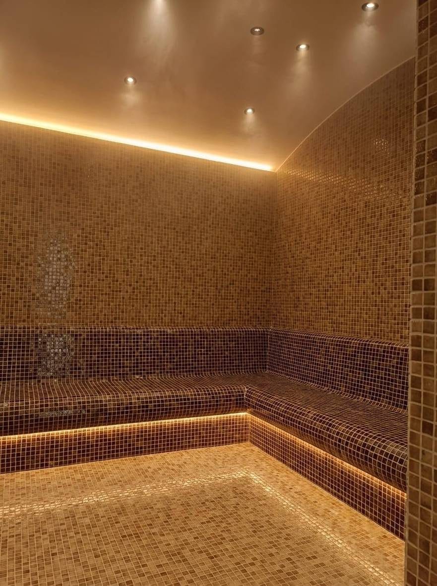 Steam room at Concorde Resort, Kyrenia: warm gold and brown glass mosaic on the walls and an L-shaped bench, a curved ceiling with recessed lights and a lit line under the bench edge