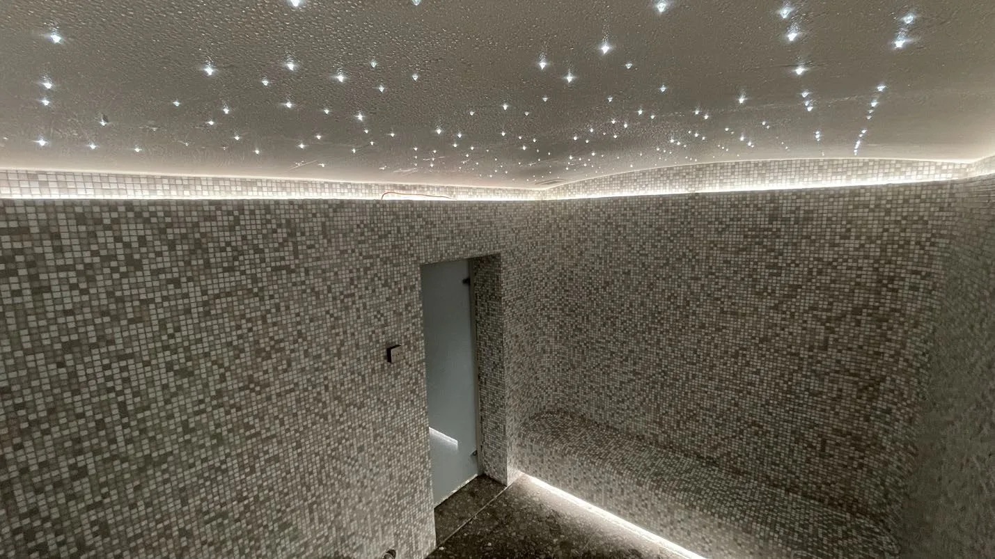 Steam room at the Diplomatic Club in Doha: pale grey mosaic on the walls and bench, a lit line along the bench edge and a ceiling scattered with fibre-optic star points